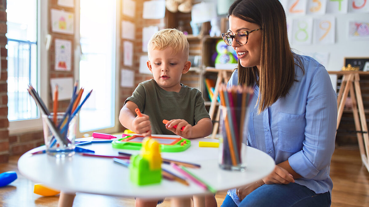 A child care provider smiling with a young child, symbolizing confidence and success after setting child care rates that support quality care.
