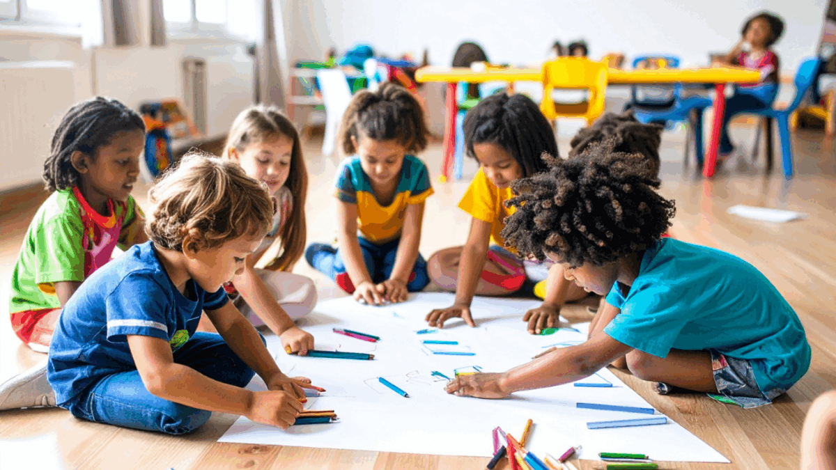 Children sitting on the ground in a daycare coloring