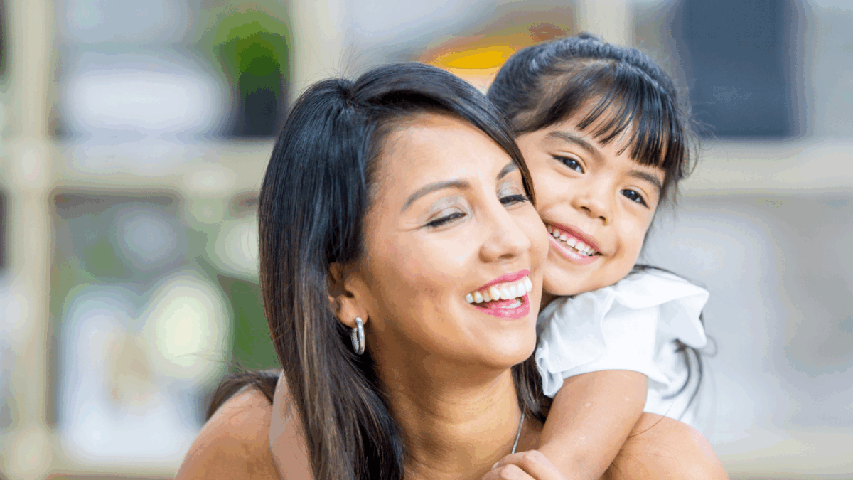 A mother smiling with her daughter on her back smiling.